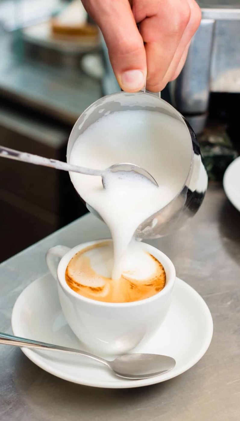 Barista in cafe or coffee bar preparing proper cappuccino pouring milk froth in a cup